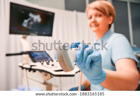 Focus on woman sonographer's hands in sterile gloves holding ultrasound transducer. Female doctor using modern ultrasound scanner. Concept of ultrasonography, medical equipment, ultrasound diagnostics
