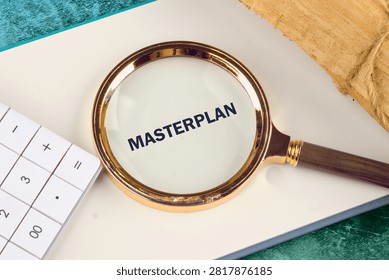 Focus on the word Masterplan through a magnifying glass placed on a white notebook next to a calculator as part of an organized business project analysis