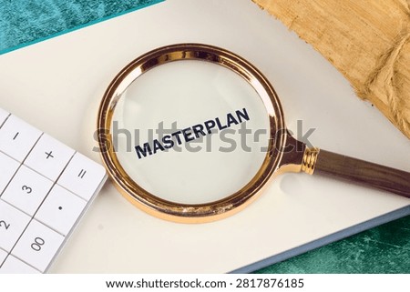 Focus on the word Masterplan through a magnifying glass placed on a white notebook next to a calculator as part of an organized business project analysis