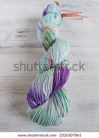 Focus selection on twisted hanks of hand dyed cotton yarn in variegated color of green and purple. Isolated on rustic white wooden background.  