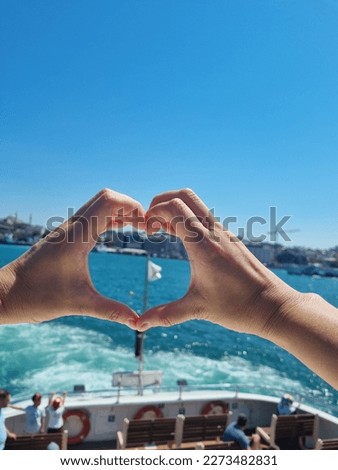 In focus using hands to make heart shape at the bosphorus cruise tour at turkiye-istanbul with out focus of flag of cruise ship at sunny day