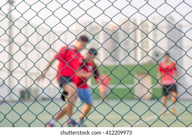 Focus Of Wired Fence And Blur Image Of People Are Playing Futsal. Exercise After Work