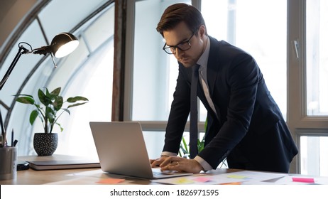 Focused 30s Male Ceo Executive In Eyeglasses And Formal Wear Using Computer Application, Preparing Online Project Presentation, Checking Information From Paper Documents With Colorful Sticky Notes.