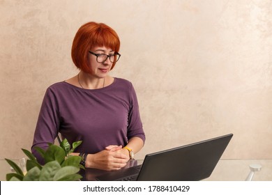 Focused 55 Year Old Woman At Home Using Laptop. Senior Stylish Entrepreneur With Notebook, Wearing Eyeglasses Working On Computer. Well Aged Mature Woman With Red Hair Working At Home. 