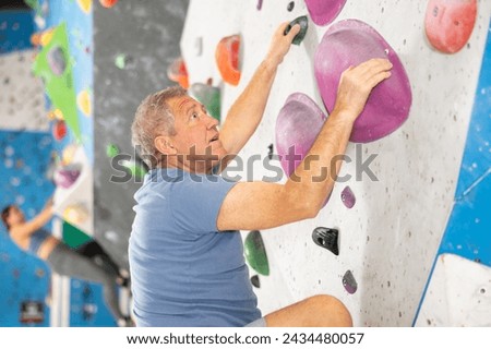 Focused active aged man climbing on bouldering wall demonstrating physical strength, technical skill, and determination.