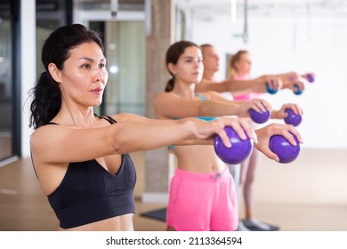 Focused Active Young Adult Woman Doing Workout With Toning Weight Balls At Group Pilates Class