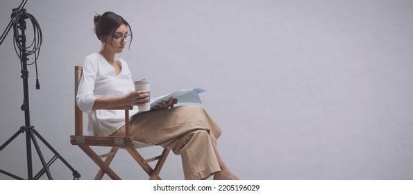 Focused Actress Sitting On The Director's Chair And Reading A Play Script, Copy Space And White Background