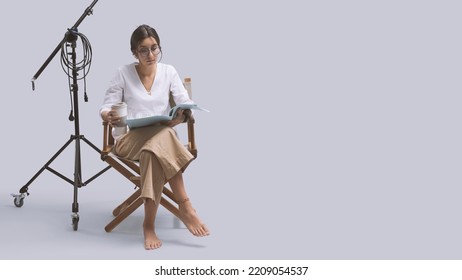 Focused Actress Sitting On The Director's Chair And Reading A Play Script, Copy Space And White Background