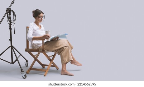 Focused Actress Sitting On The Director's Chair And Reading A Play Script, Copy Space And White Background