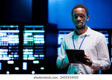 Focused admin using tablet to assess energy consumption across server rackmounts components. Employee making sure high tech data center mainframes temperature sensors are running smoothly - Powered by Shutterstock