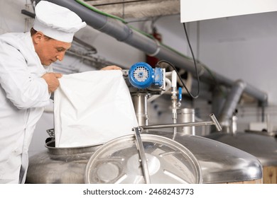 Focused adult brewer working in small brewery, pouring malted grain from bag into fermenter to produce beer.. - Powered by Shutterstock