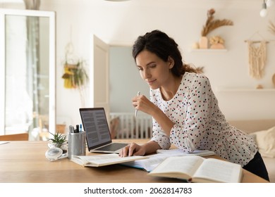 Focused adult female student doing homework, reading books at laptop, taking notes. New mother learning online from home, getting new occupation, preparing for college test. Education concept