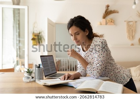 Focused adult female student doing homework, reading books at laptop, taking notes. New mother learning online from home, getting new occupation, preparing for college test. Education concept