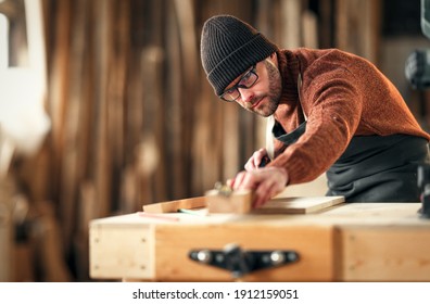 Focused adult male woodworker in apron and knitted gat cutting wooden plank while working in carpentry workshop - Powered by Shutterstock