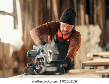 Focused adult woodworker in apron and protective gloves using electric grinder while polishing wooden detail in craft workshop - Powered by Shutterstock