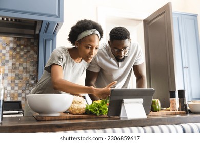 Focused african american couple preparing meal together using tablet in kitchen. Cooking, healthy lifestyle, recipe, communication, togetherness, food and domestic life, unaltered. - Powered by Shutterstock