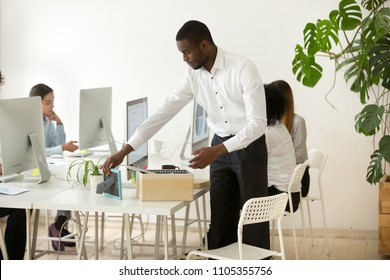 Focused African American Employee Unpacking Box With Personal Items On First Work Day At New Workplace, Putting Frame On Office Desk, Black Newcomer Setting In Coworking Space Getting Comfortable