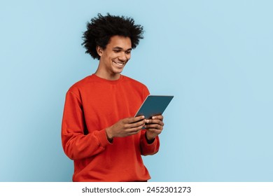 A focused african american guy engaged with a digital tablet, isolated on a blue background, representing modern connectivity - Powered by Shutterstock