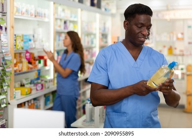 Focused African American Male Pharmacist Working In A Pharmacy Is Carefully Studying The Composition Of A Hair Care Product ..while Standing In The Trading Floor