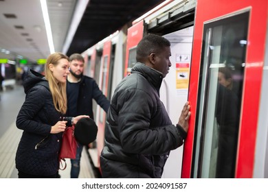 Focused African American Man In Warm Jacket Getting On Modern Subway Car With Other Passengers. Concept Of Daily City Trips