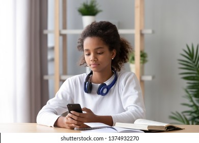 Focused African American Teen Girl Using Phone, Distracted From Homework, Looking At Screen, Lazy Schoolgirl Chatting In Social Network Instead Of Doing School Tasks, Children Gadget Addiction