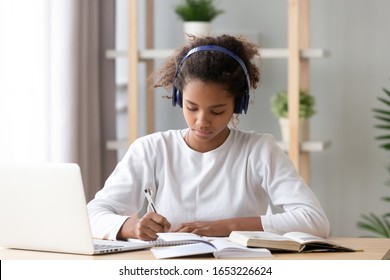 Focused african american teenage girl wearing headphones writing notes study with laptop and books, serious black female high school teen student listening audio course or music while doing homework - Powered by Shutterstock