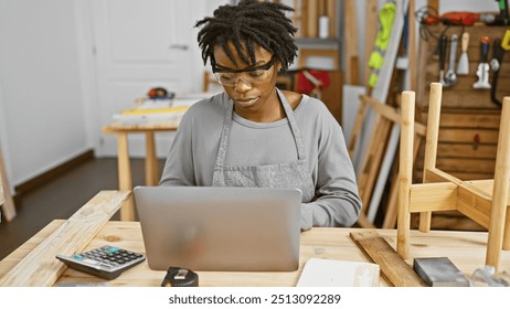 Focused african american woman with dreadlocks working on a laptop in a woodworking workshop. - Powered by Shutterstock