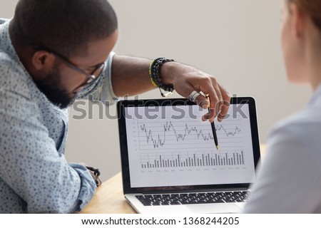 Focused african analyst showing client or colleague annual financial report analyzing business data on laptop screen using software for digital graphic statistic analysis, economic market graphs 