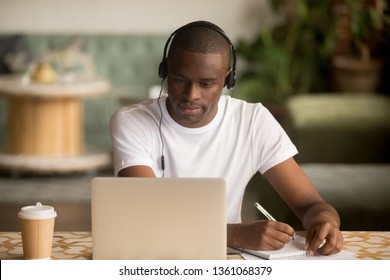 Focused African Man Wearing Headphones Watching Webinar Training Making Notes Study Online Learning Language On Computer, Black Male Student Looking At Laptop Elearning In Internet Write Information