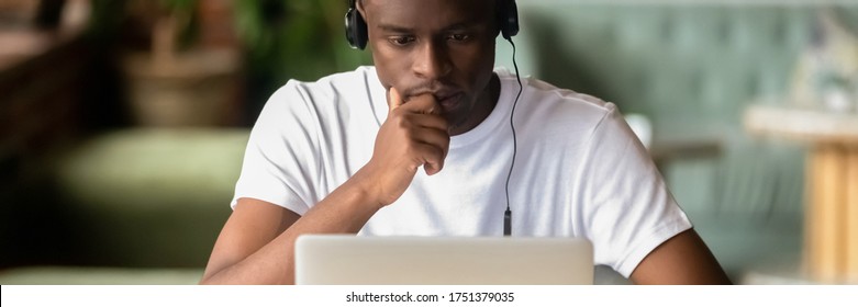 Focused African student wear headphones studying on-line do exercise using laptop, watching video, learning language, self-education, e-study concept. Horizontal photo banner for website header design - Shutterstock ID 1751379035