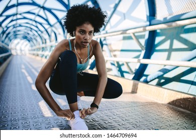 Focused african woman in fitness wear tying her shoelace. Fitness woman tightening her shoes before a sprint.