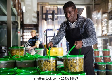 Focused African-American Man Working In Food Producing Factory, Arranging Plastic Buckets With Pickled Olives