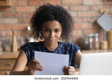 Focused Afro American student girl receiving important paper letter, acceptance notice from college, university, paid loan confirmation from bank, bill for insurance fee, tax payment. Paperwork