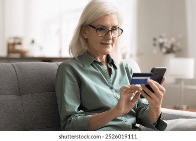 Focused aged 65s woman buying goods and services on internet, holding smartphone and credit card making purchases on e-commerce websites, buying digital content, ordering groceries and household items - Powered by Shutterstock