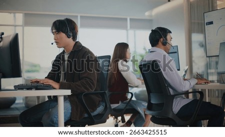 Focused Asian agent at tech support call center provides professional customer service. male operator helps client with problem working on computer in modern office