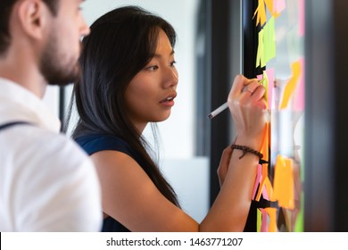 Focused asian business woman mentor coach leader writing idea or task on post it sticky notes on glass wall, serious team people developing work plan in creative corporate office at stand up meeting - Shutterstock ID 1463771207