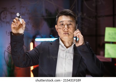 Focused Asian Male Ceo Manager In Formal Wear Writing On Glass Board With Colorful Sticky Notes And Talking Phone, Working With Project In Modern Night Office. Creative Thinking, Startup Plan Concept