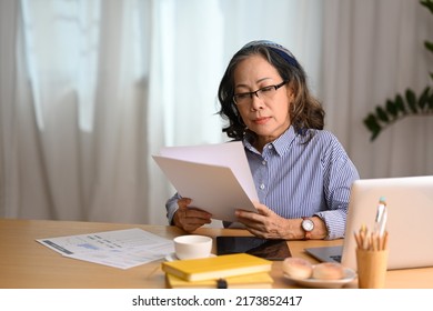 Focused Asian Mature Lady Wearing Glasses Using Laptop And Managing Household Finance