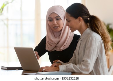 Focused Asian Muslim Female Mentor Teacher Teach Caucasian Intern Worker Learning New Skills Explaining Computer Software Work Together At Modern Workplace, Apprenticeship Internship Course Concept