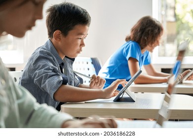 Focused Asian school boy using digital tablet at class in classroom. Attentive junior school student learning online virtual education digital program app tech during stem computer science lesson. - Powered by Shutterstock