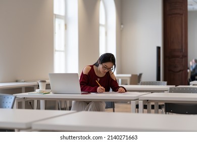 Focused Asian Student Prepare For Coursework In Library. Concentrated Girl Writing Speech For Graduation Event At University, High School Or College Campus. Young Woman Studying Alone In Empty Class