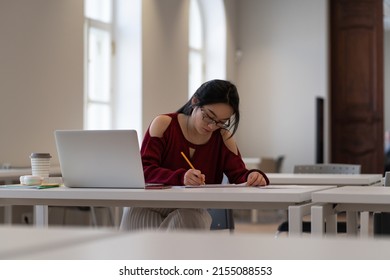 Focused Asian Student Prepare For Coursework In Library. Concentrated Girl Writing Speech For Graduation Event At University, High School Or College Campus. Young Woman Studying Alone In Empty Class