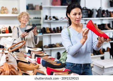 Focused Asian Woman Who Came To A Shoe Store For Shopping, Chooses Ballet Flats, Carefully Examining Them