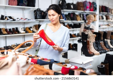 Focused Asian Woman Who Came To A Shoe Store For Shopping, Chooses Ballet Flats, Carefully Examining Them