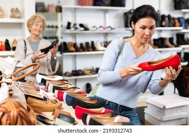 Focused Asian Woman Who Came To A Shoe Store For Shopping, Chooses Ballet Flats, Carefully Examining Them