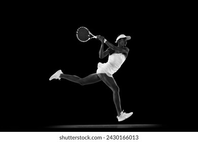 Focused athlete in tennis gear executing powerful forehand swing against black studio background. Monochrome filter. Concept of sport, active lifestyles, tournaments and events, energy, movement. - Powered by Shutterstock