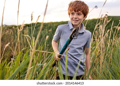 Focused, Attentive Little Redhead Boy Catch Fish On River Holding Fishing Rod In Hands, Caucasian Child Standing In Field Near Lake, In Nature, Countryside. Copy Space, Portrait