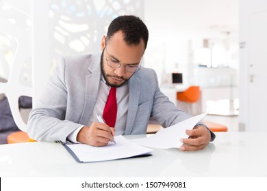 Focused auditor checking document. Business man wearing suit and eyeglasses, signing contract. Document expertise concept