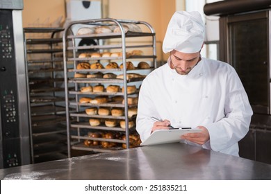 Focused baker writing on clipboard in the kitchen of the bakery - Powered by Shutterstock