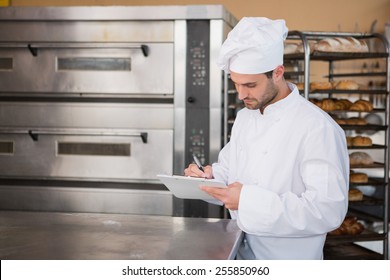 Focused baker writing on clipboard in the kitchen of the bakery - Powered by Shutterstock